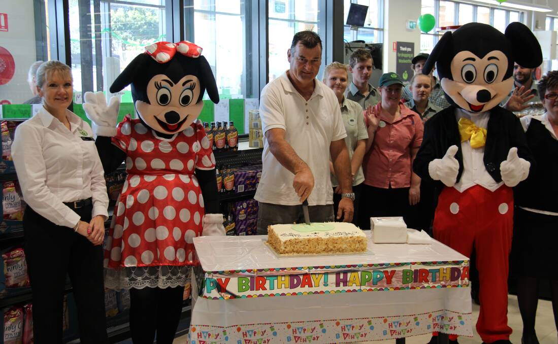 HAPPY BIRTHDAY: Tim Preo, Bermagui Woolworths' very first customer from 12 months ago, cuts the cake during first birthday celebrations last week.