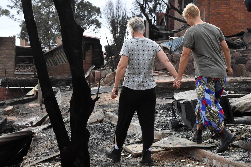 EMOTIONAL: Tathra residents Deb Naeve and Ingrid Mitchell wander through the burnt out remains of their Wildlife Drive home. Picture: AAP, Dean Lewins