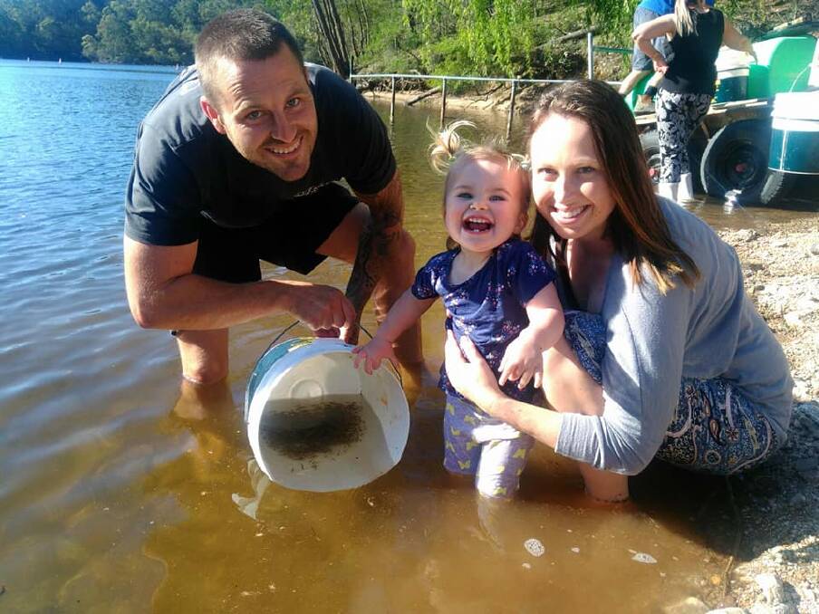 FUN, FISHING AND FAMILY: Rahki Dummet releases bass fry into Brogo Dam with some help from dad Tim and mum Steph. Photo: Supplied.