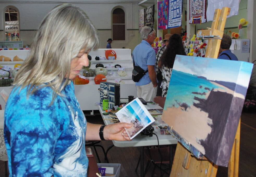Nicky Hall paints a Bermagui beach scene as part of the demonstration of crafts in the gallery.