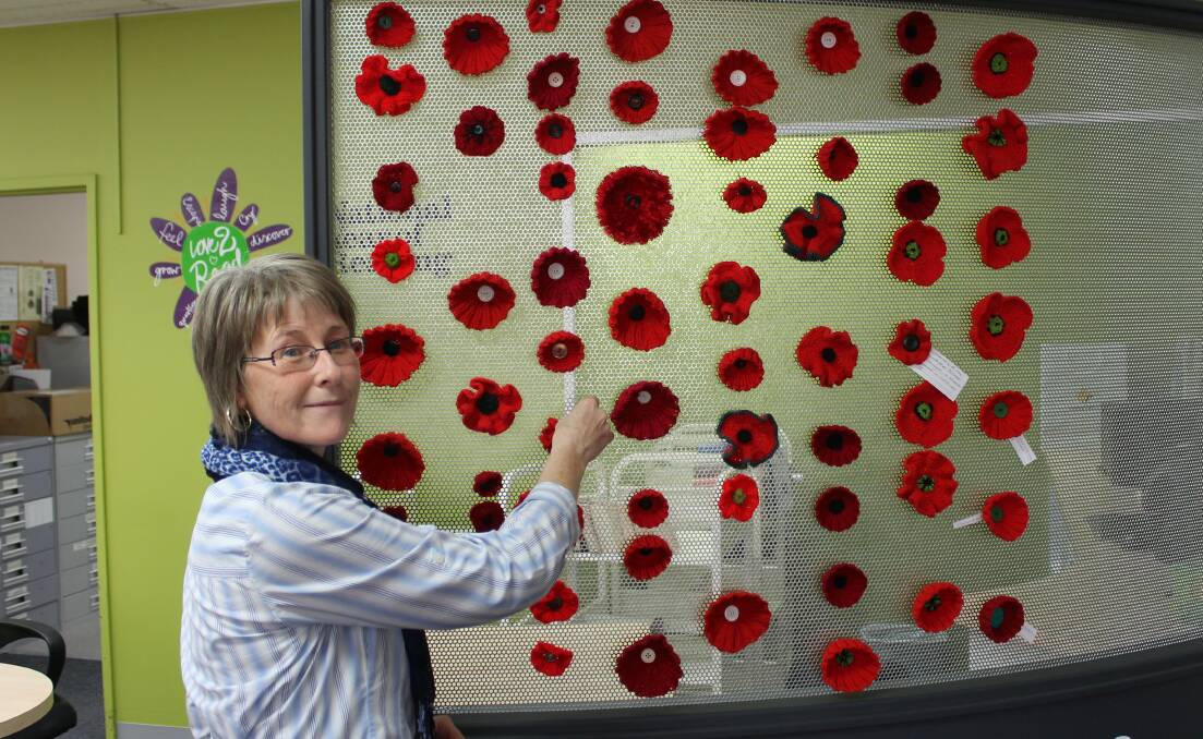 Librarian Linda Albertson hangs up one of the red poppies in the Bega Library.