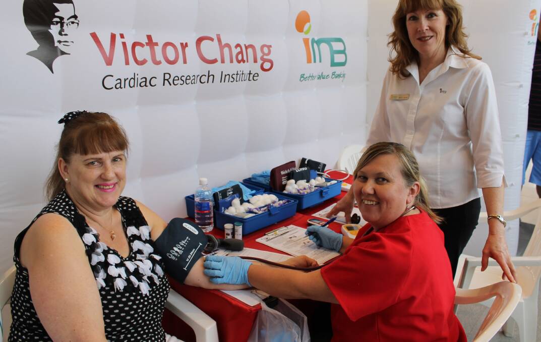 Patricia Hinves (left) visits the Victor Chang Cardiac Research Institute Health Check Booth to have her blood pressure checked by nurse Sanya Kirkwood, watched by IMB’s Mary-Anne Carroll (right).
