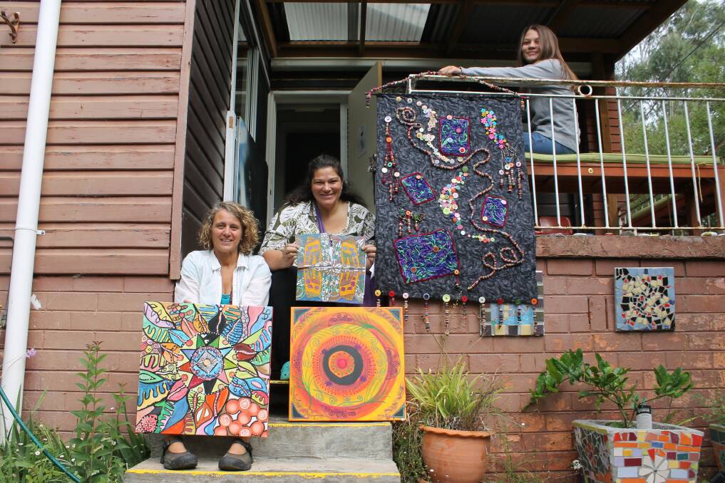 Preparing for International Women’s Day events in Bega, Kate Stead (middle) sits with her collaborative piece House24/7 and her daughter Tazmin Bay (right) who holds a work by Phyllis Furby of Cobargo, while coordinator of the Bega Women's Resource Centre Gabrielle Powell (left) holds a painting by Carmen Goodall beside a piece by Christine Quinton. 