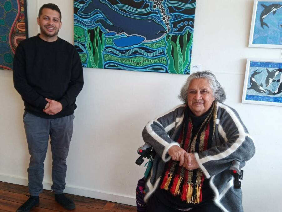 Aunty Colleen Dixon all smiles in front of Robben Dixon's artwork (the orca paintings) and beside artist Marcus Mundy. Photo supplied.