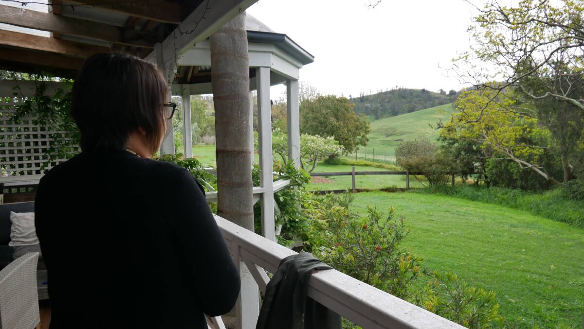 Karyn Thompson stands on the veranda facing out towards the side of her property, now lush green, more than 20 months on from NYE 2019-2020 during the Black Summer bushfires. Picture: Ellouise Bailey 