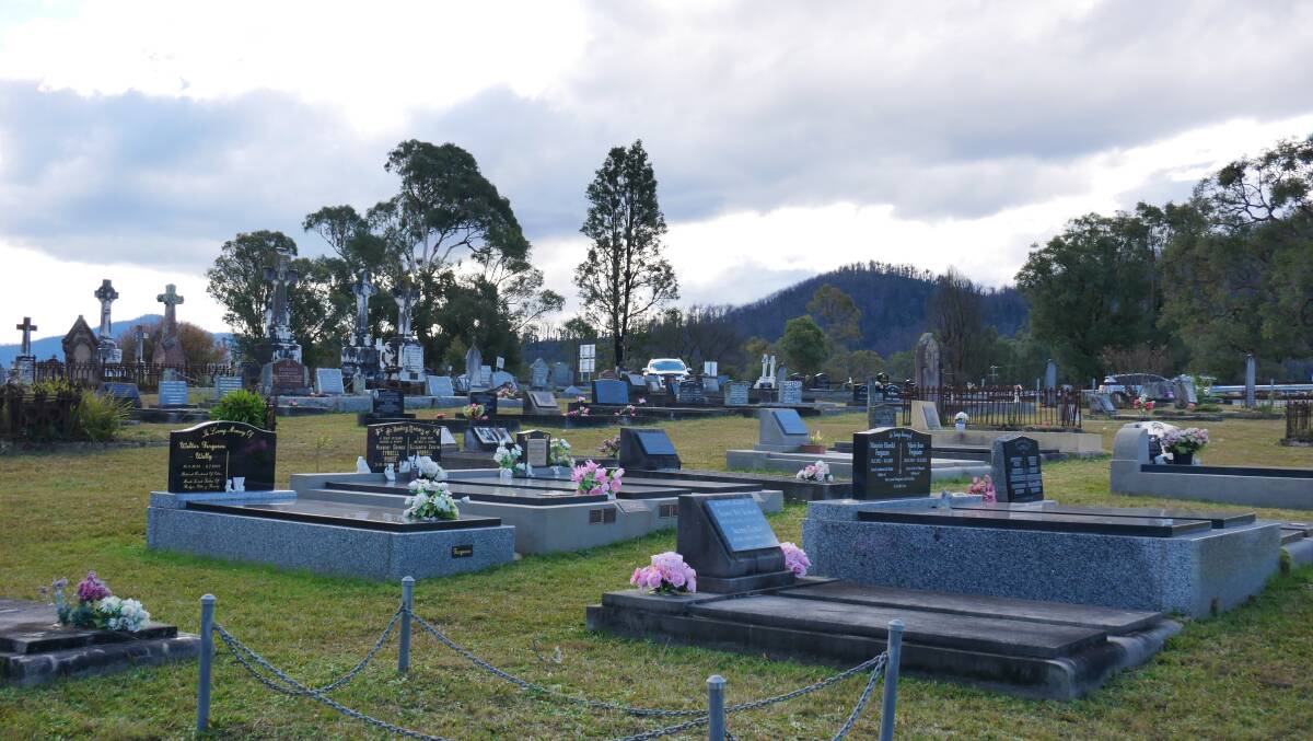Gravesites at the Cobargo cemetery which came very close to being burnt during the bushfires. The burnt skeletal trees in the background loom over the graves. 