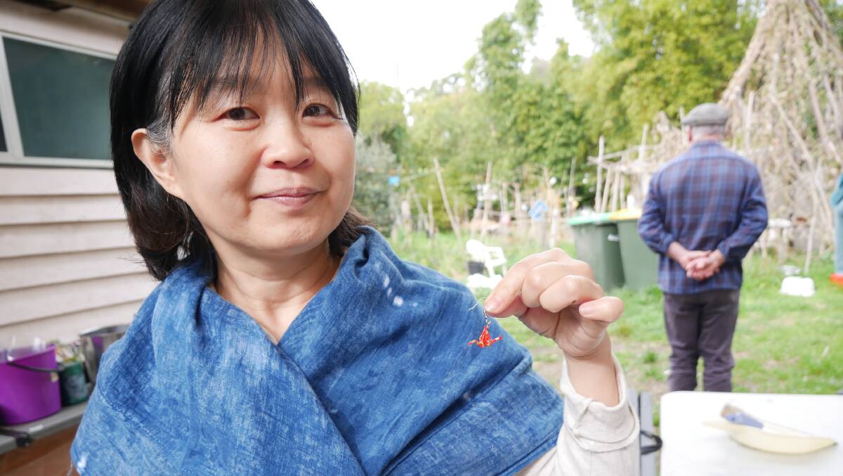 Reiko holds one of her tiny origami earrings and wears a reclaimed scarf that she has used indigo to tie dye. 
