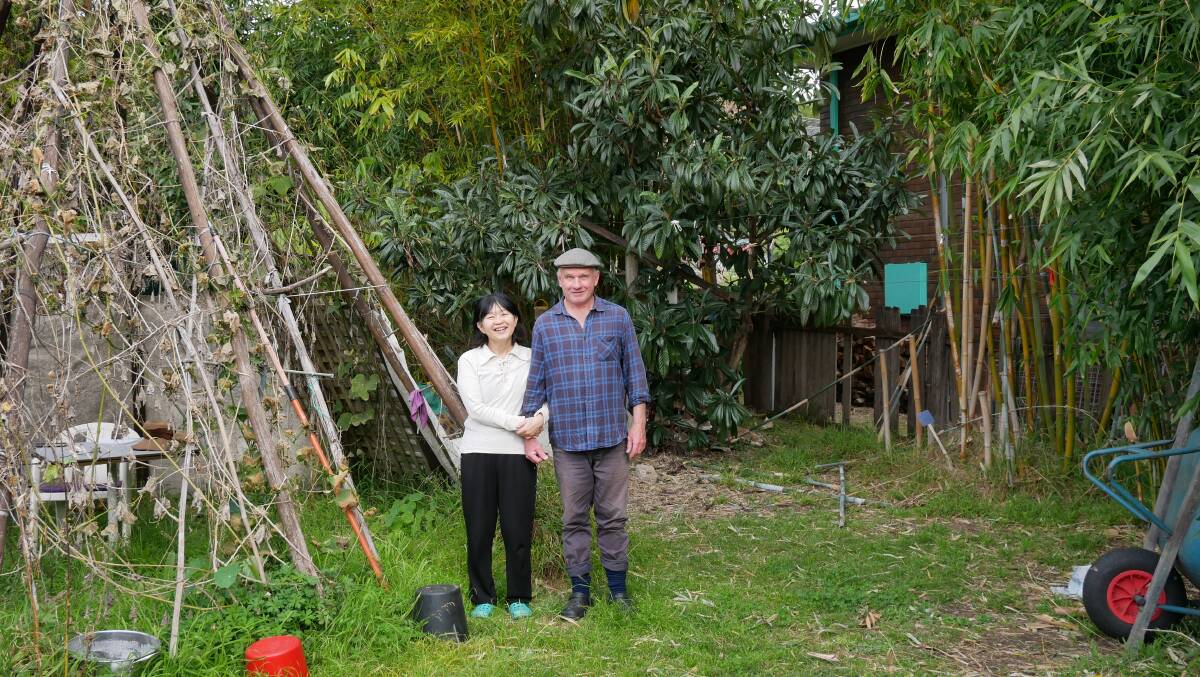 Reiko Okamoto Healy with her husband Wayne Healy in their backyard. To their left is a bamboo teepee which is covered in choko vines. 