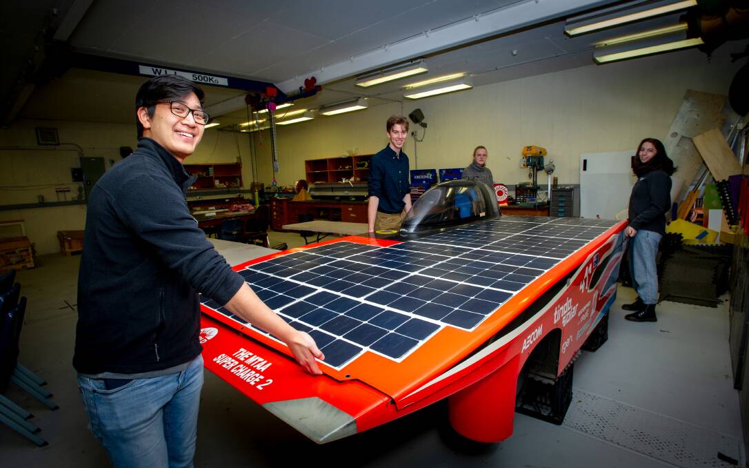 ANU Solar Racing team members David Lim, Isaac Martin, Caitlin Lovejoy and Rebecca Craine place the top on their 2019 solar car. They're working on a new and improved model that will have three wheels and a super thin battery. Picture: Elesa Kurtz