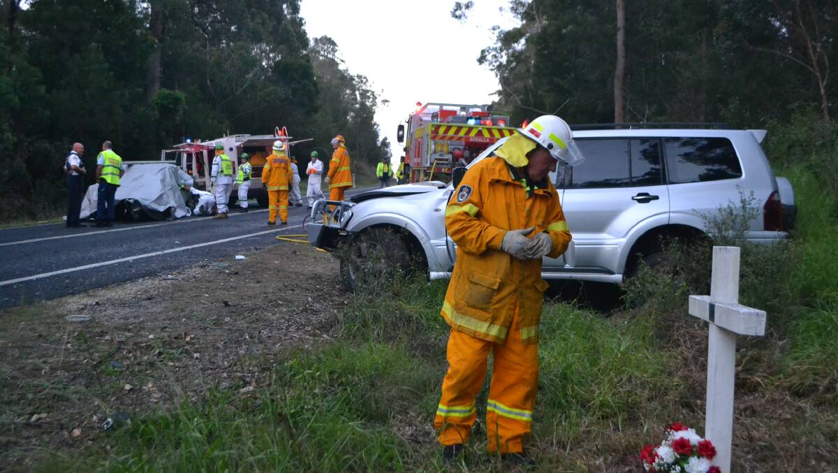ONCE AGAIN: An emergency worker at a highway crash north of Bodalla in April 2017 examines a previous memorial.