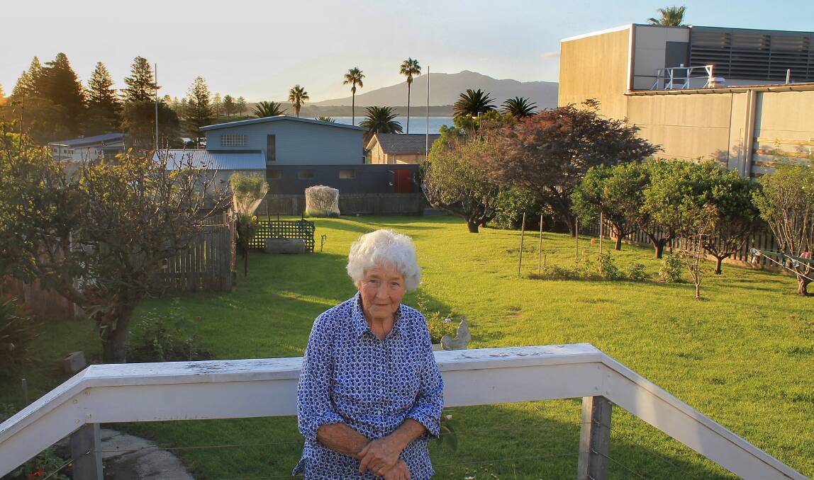 BIG CHANGE: Gloria Sherwin stands in her backyard. On the right is the side of Bermagui Woolworths, while behind her the two poles either side of the blue house show how high the three-storey home will be. Picture: Albert McKnight 