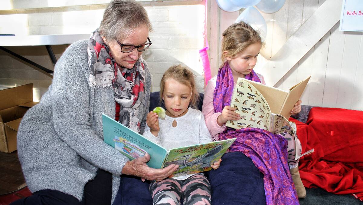 KIDS CORNER: Bega Rotary's Margaret Taylor reads to Felicity Ireland while her sister Victoria is engrossed in one of the many books on sale at last year's winter book fair. Picture: Alasdair McDonald