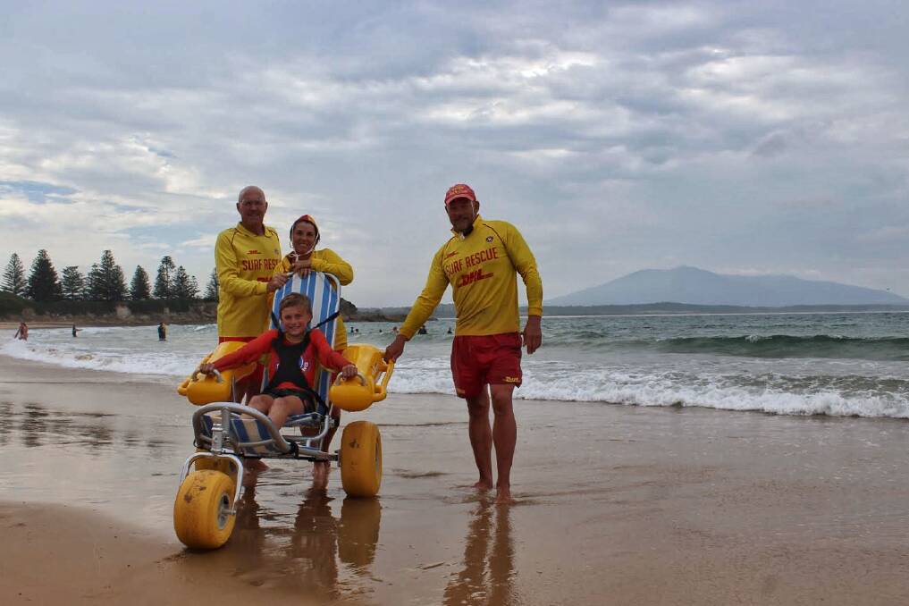 ALL IN: Bermagui Surf Life Saving Club president Bruce McAslan, secretary Cheryl McCarthy and captin Andrew Curven test out their new beach-accessible wheelchair with Nipper Zane Curven.