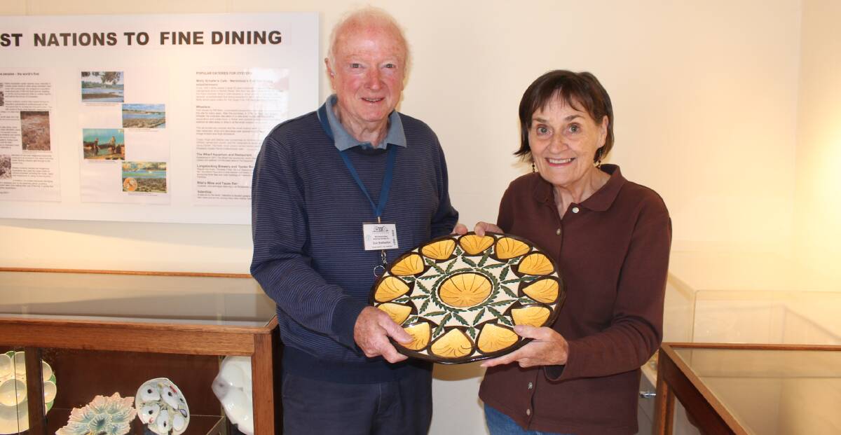 President of the Merimbula Historical Society Don Bretherton with his wife Liz, hold one of the plates from Trevor Kennedy's collection.