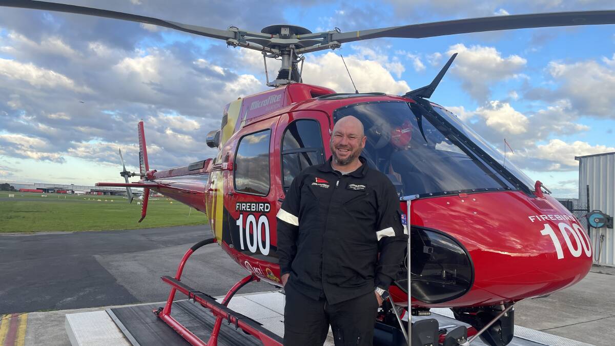 Pilot Adam Cassin pictured with the helicopter he spent so much time in during Black summer. Picture supplied