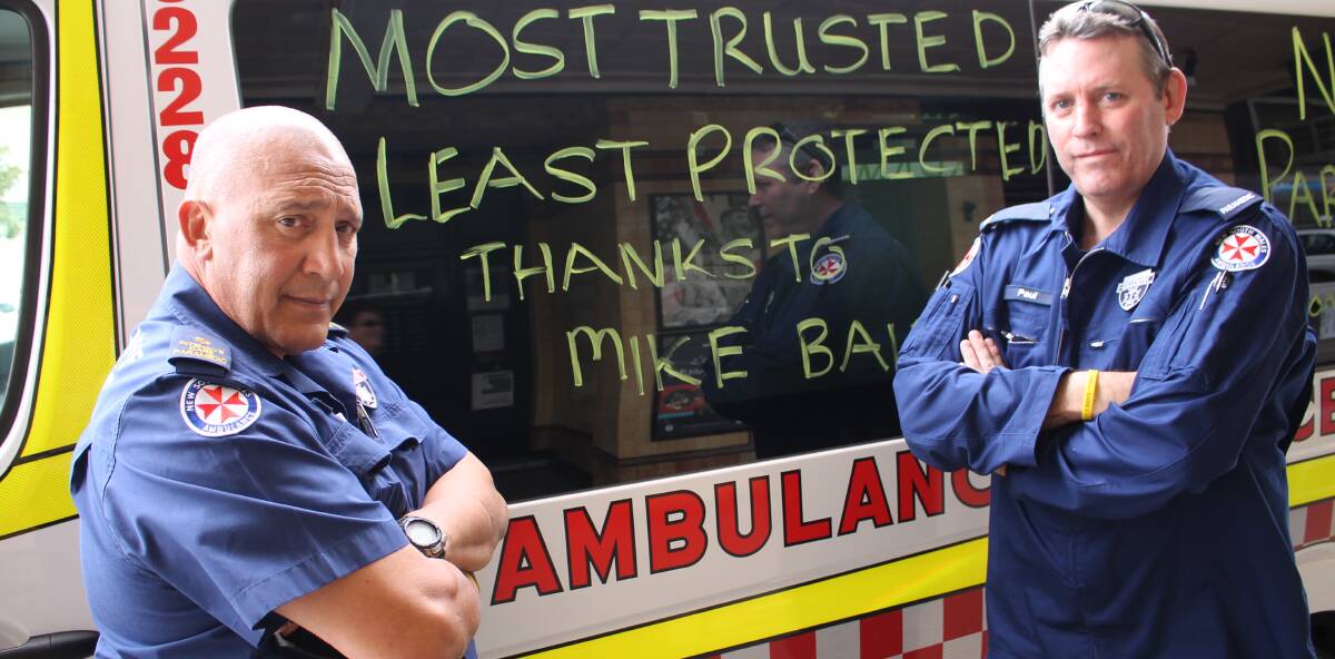 PROTESTING CUTS: Bega Ambulance Station's Rhys Tamatea and Paul Beard show one of the signs on the station's vehicles. Picture: Albert McKnight