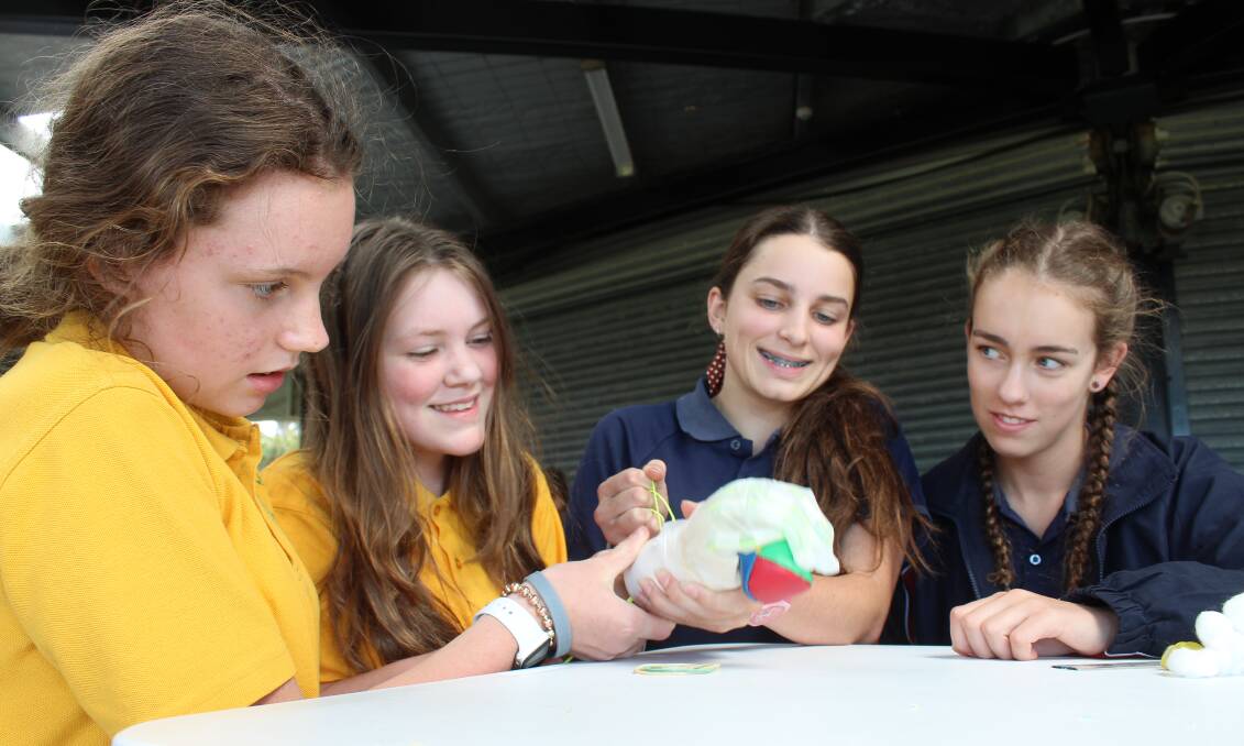 Grace Clarke and Charlotte Porter of Year 8 at Saint Patrick's Parish School Secondary Campus in Cooma pick up a ball with a bionic hand they built with Liliana Watters and Isabelle Pamplin of Lumen Christi Catholic College. 