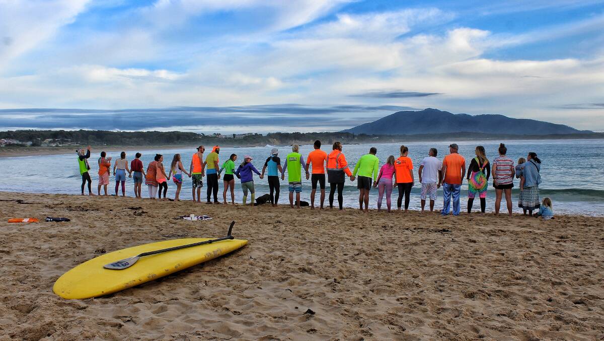 UNITED: People attending OneWave in Bermagui on March 22 hold hands for a moment's silence before jumping into the water together. 