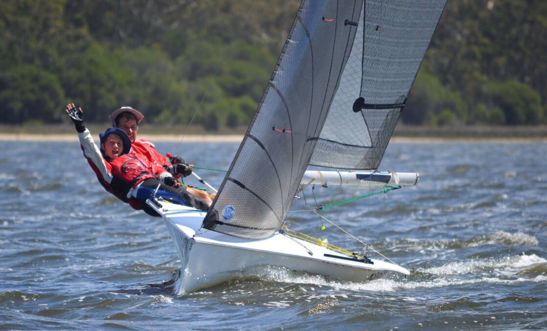 Joyous sailing: Jarrah Dorrough waves to the camera as Dad, Josh, keeps their NS14 powering along during races at Wallagoot. Picture: supplied. 
