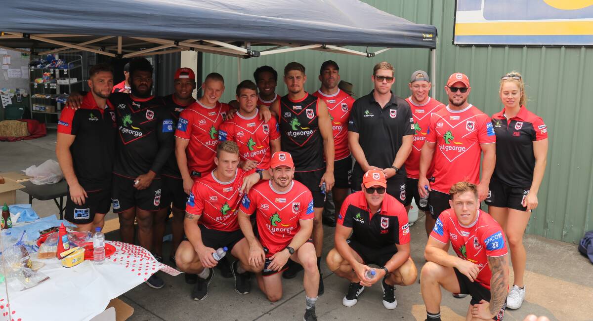 Players, coaches and staff from the St George Illawarra Dragons pause for a quick photo while manning the barbecue in Cobargo on Wednesday. 
