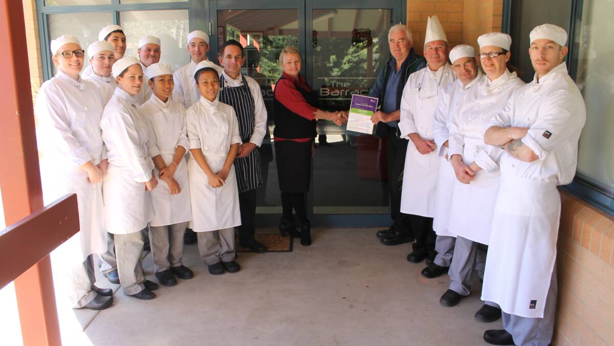 Bega Valley Shire Council environmental health coordinator Greg O’Donnell hands TAFE Illawarra Bega campus Tourism and Hospitality head teacher Deirdre Jory a 5-star Scores on Doors accreditation for The Barracks Restaurant. They are flanked by Bega TAFE first year apprentice commercial cookery students, commercial cookery teacher Michael Burbidge (fourth from right) and class preparation assistant Dave Dunn (seventh from right).