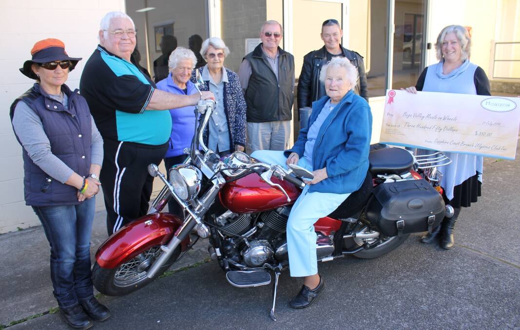 Isobel Bobin revs the motor on the bike 'Ruby', surrounded by (from left) Kerrin Daw, Ulysses Sapphire Coast secretary Bruce Bearman, Meals on Wheels Monday Social Club members Patricia Waterson and Lola Boller, Meals on Wheels board of directors secretary Tony Toussaint, Ulysses Sapphire Coast president Kate Spears and Meals on Wheels manager Fiona Scott. 